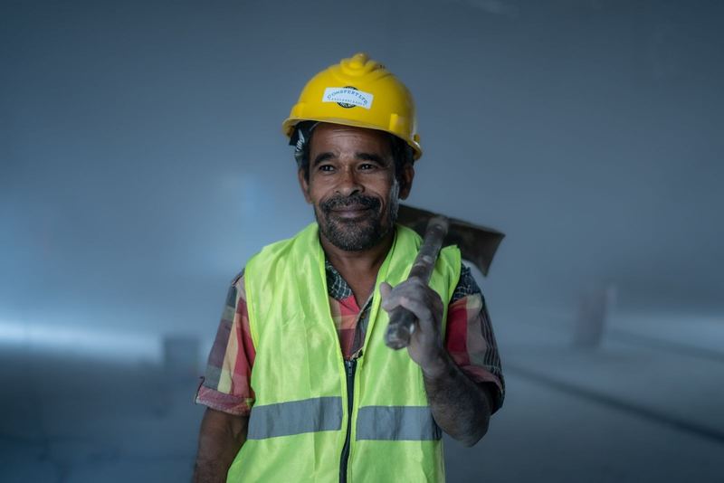Smiling construction worker in safety gear holding a tool indoors. Professional and industrial theme.